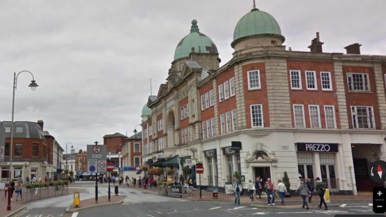 A street view image of Mount Pleasant Road in Tunbridge Wells in the day time, showing a Victorian neo-palladian building, traffic and the bus gates area near the town centre.