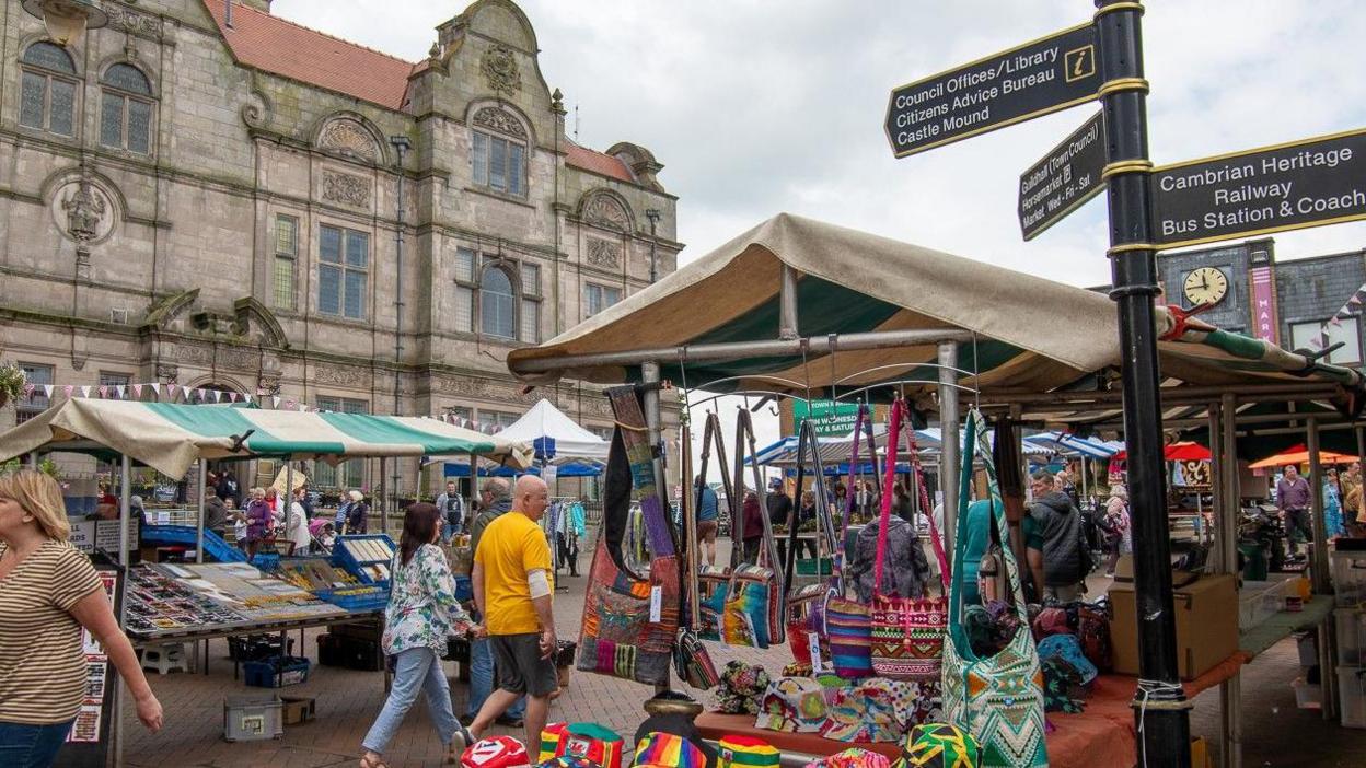 Oswestry's Guildhall, a three-storey building, is in the background. Market stalls and some people are in the foreground.