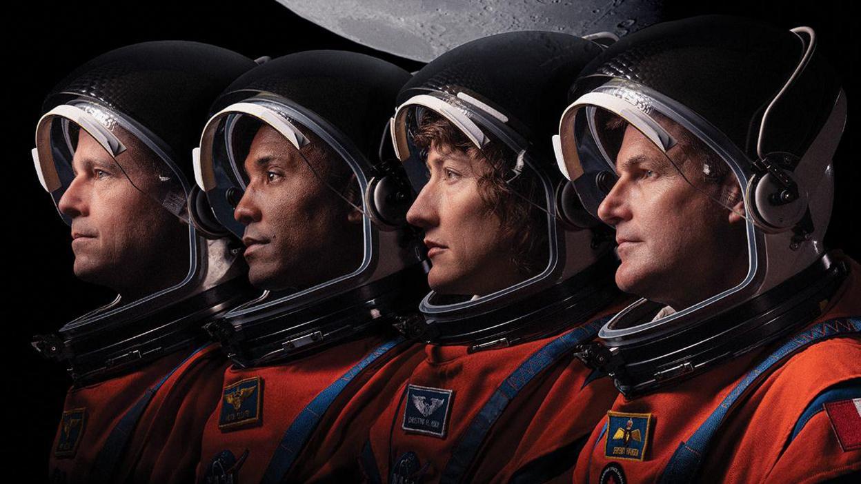 The Artemis II astronauts shown in a line with their space suits and helmets on.