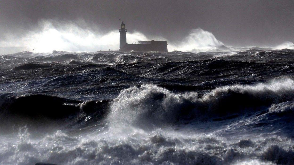 Giant dark blue waves hit the lighthouse wall at Whitehaven when a storm hit the area in 2014. It is a very dark and stormy day.