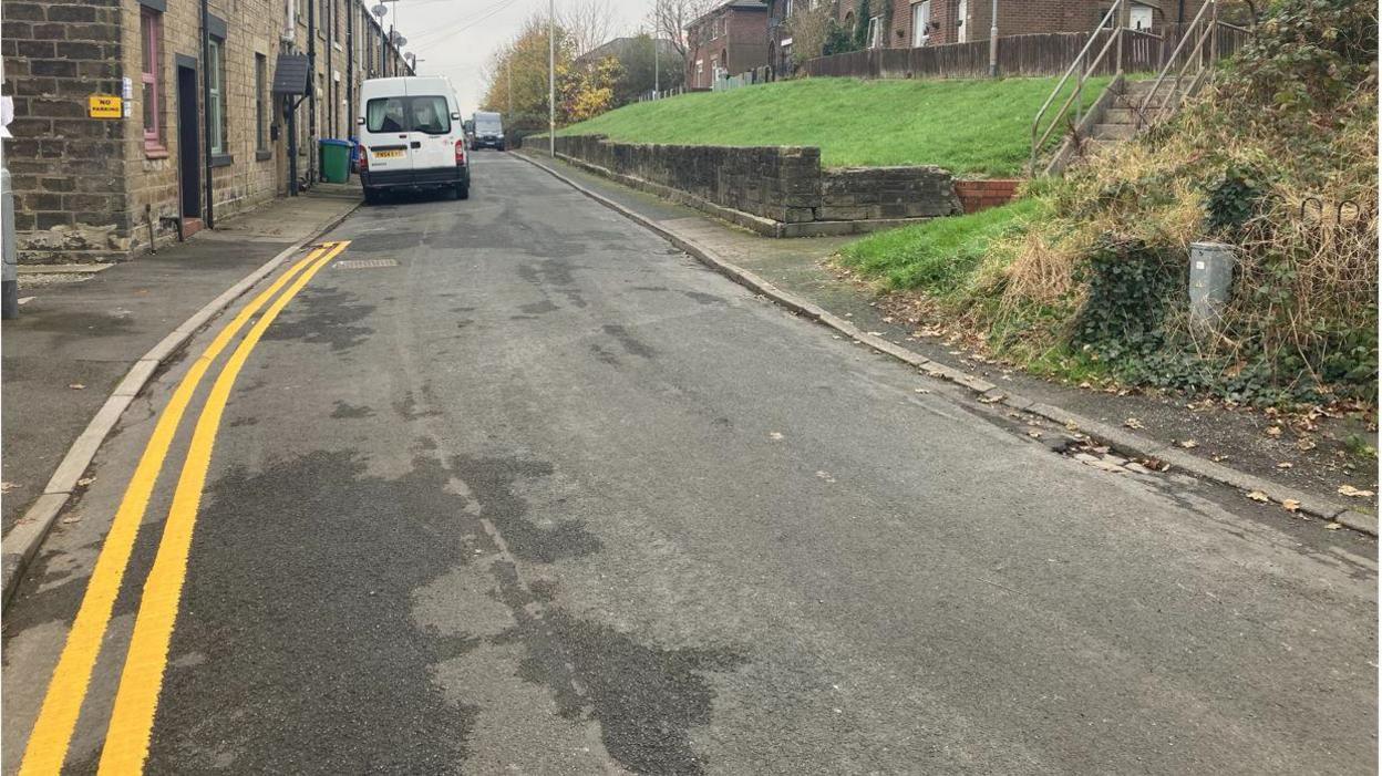 Double yellow lines running along Major Street in Milnrow. Homes line both sides of the street and several cars are parked up.