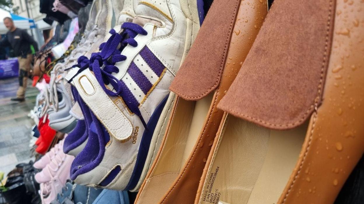 A close-up of different shoes, they are vertical, there are brown women's shoes in the foreground, with white and blue trainers behind.