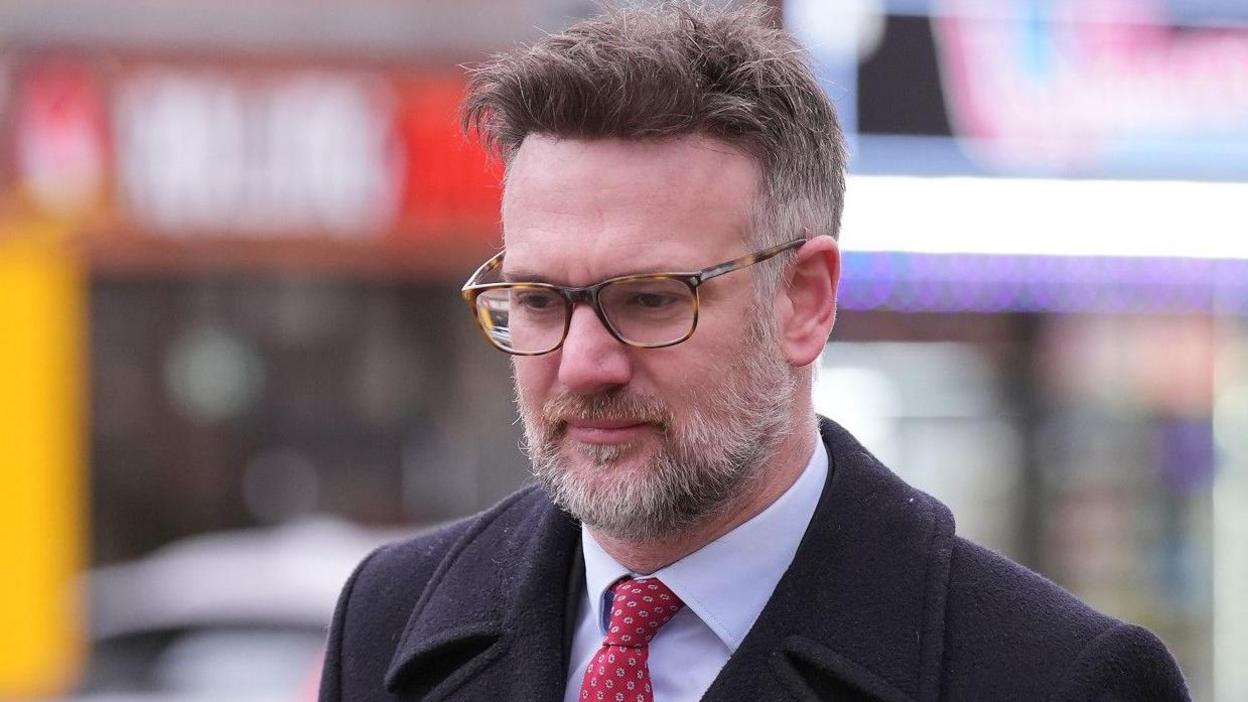 Charles Hanson in a suit and tie walking beside a busy road