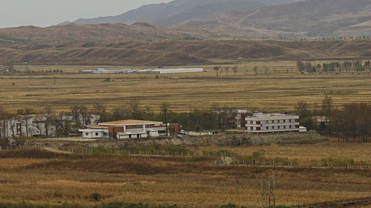 A view of the North Korean countryside, as seen from the Chinese border in Fangchuan, shows acres of land, with two large buildings in the foreground and hills in the background