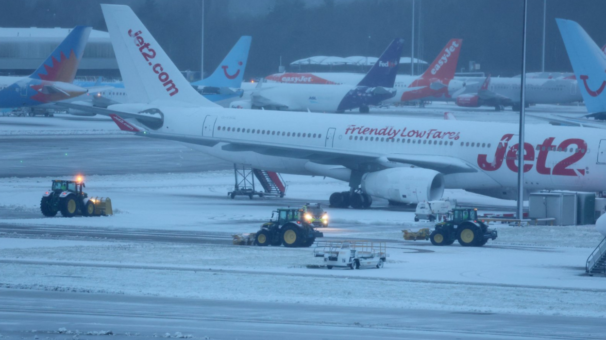 Staff use tractors to help clear snow from around aircraft after overnight snowfall caused the temporary closure of Manchester Airport