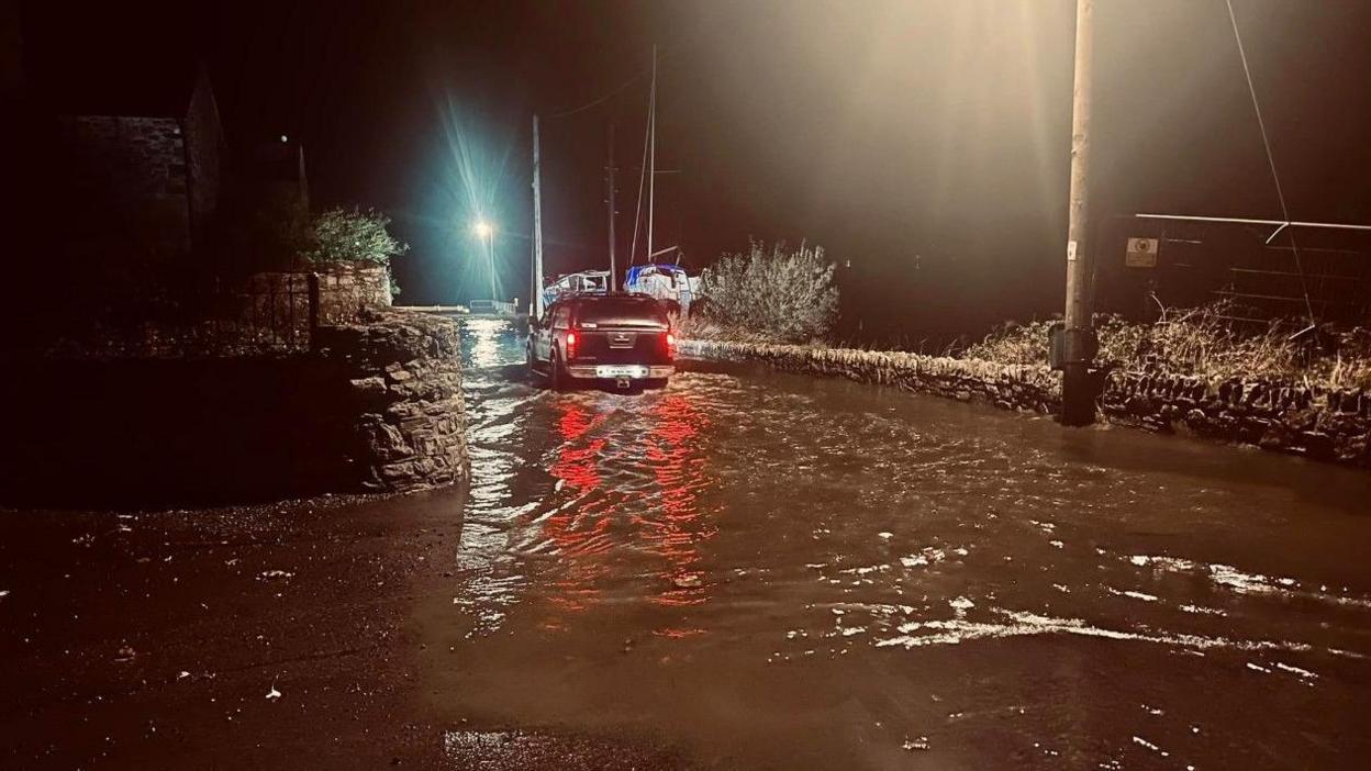 A black jeep is pictured driving through flood waters in Ramelton, County Donegal, at nighttime. 