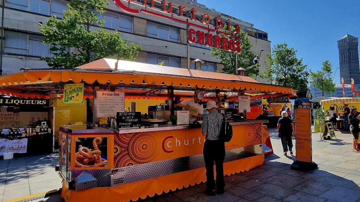 A large bright orange food stand has an illuminated red sign above it which reads Churtopia Churros.