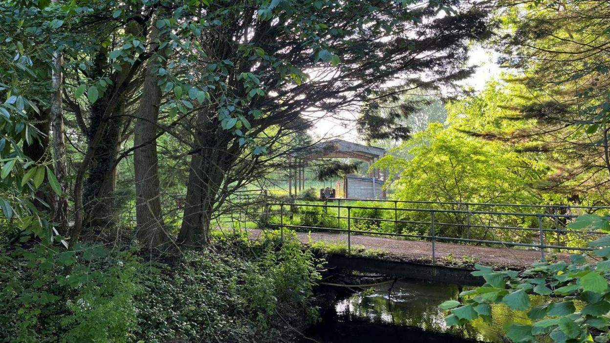 A metal bridge above a river, with a farming shed visible in the background