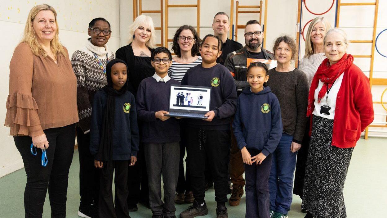 Pupils at May Park Primary and adults involved in the making of the UWE video face the camera in a group shot while holding a laptop showing the animation on 