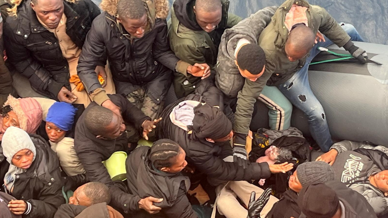 African migrants rugged up in winter coats surround a baby just minutes after it was born on a dinghy off the coast of Spain's Canary Islands