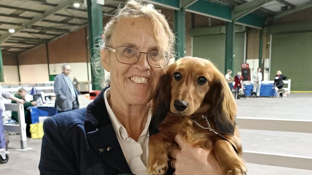 A woman wearing a blue blazer holds her dog close to her face in an embrace.