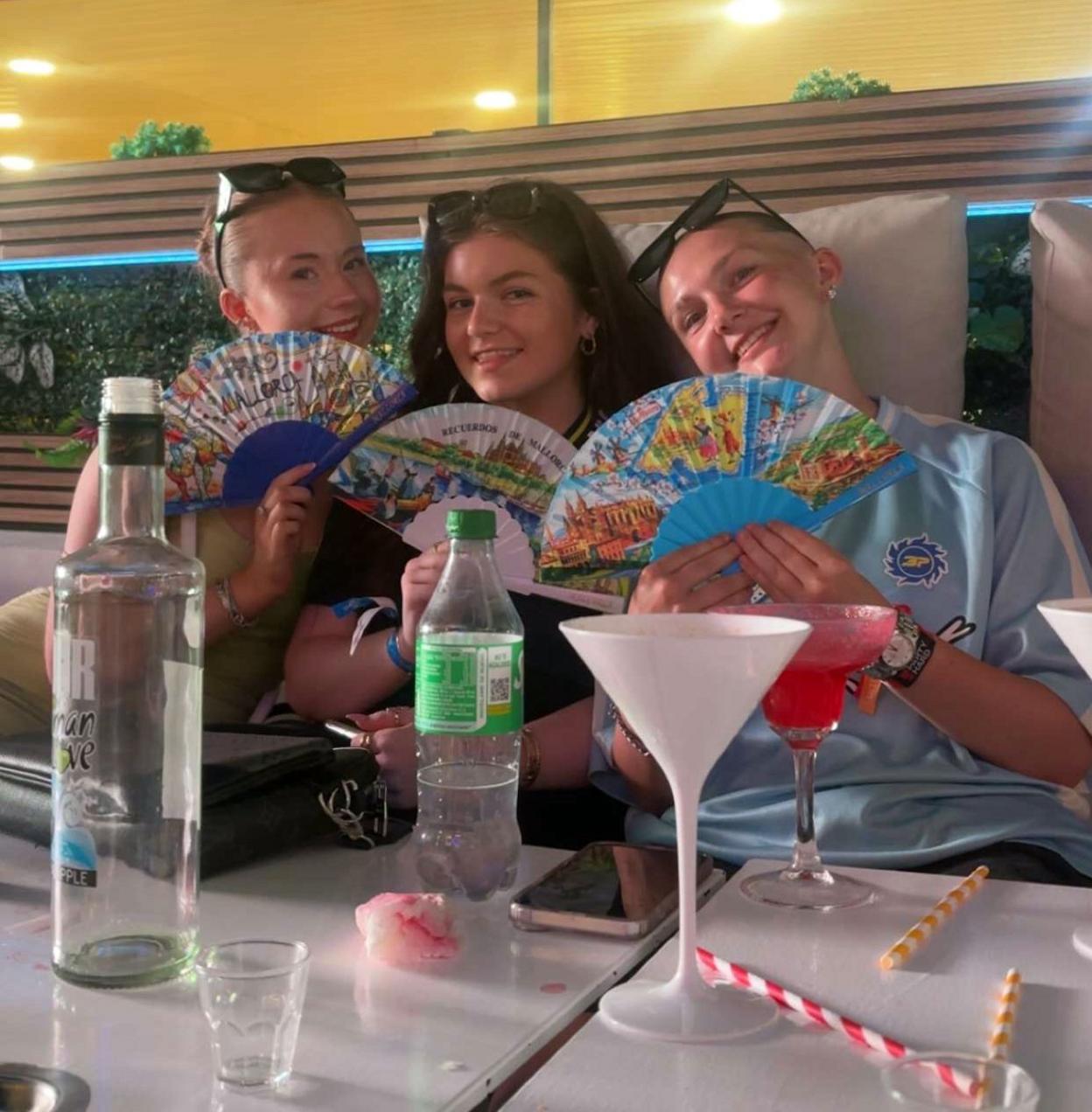 Three young women sitting in a bar, holding paper fans