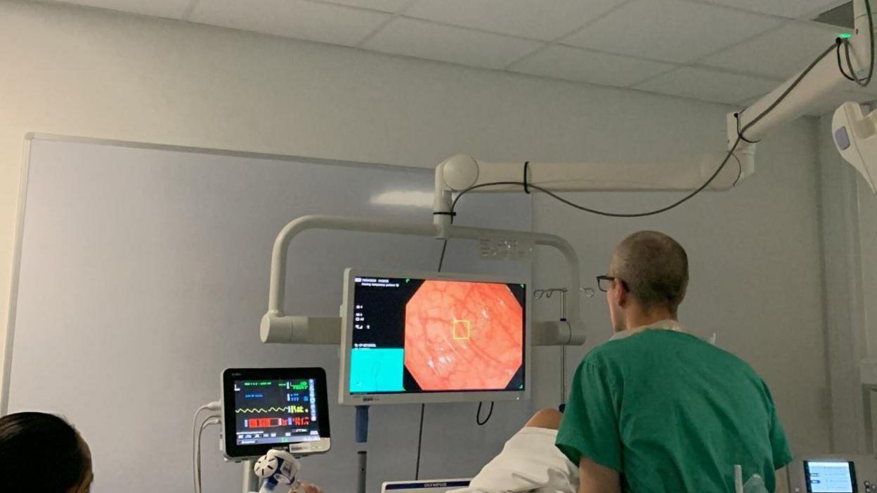 A doctor looking at a monitor which shows the inside of a patient's bowel. A yellow square is on the screen highlighting a polyp.