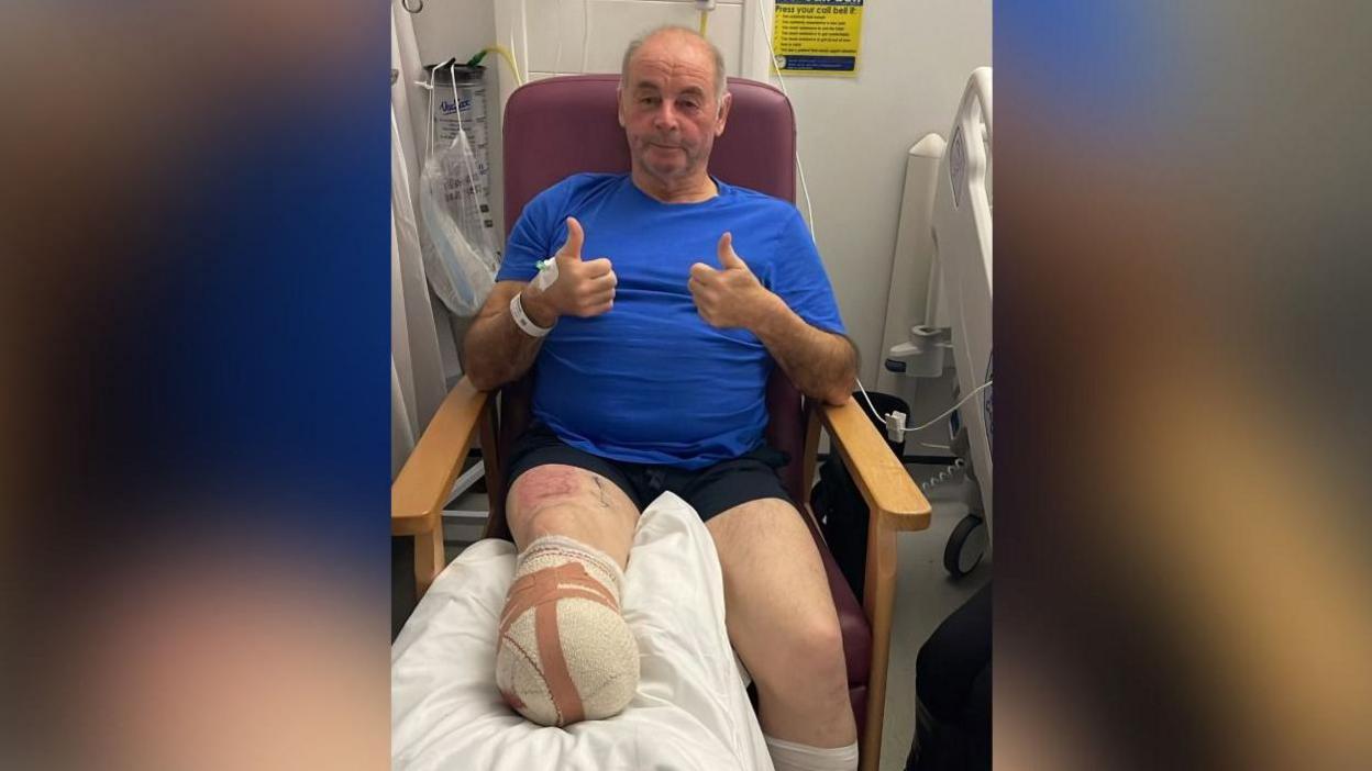 Llun o Alun mewn cadair yn yr ysbyty a rhwymyn ar ei goes