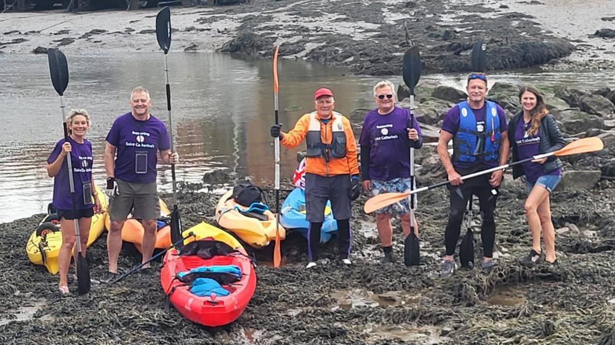 A group shot of Barry Samples and his family, holding kayak paddles and standing beside kayaks.