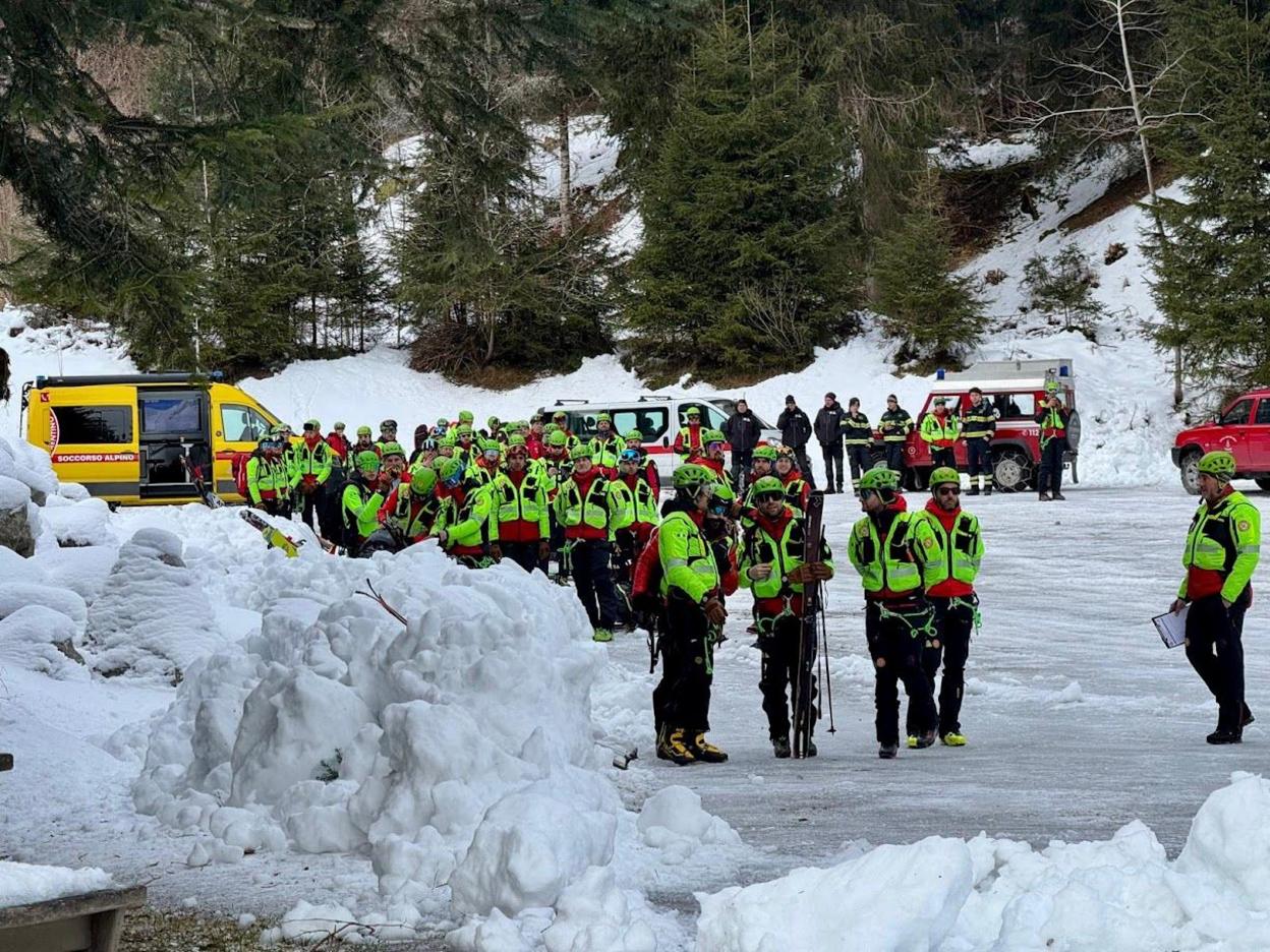 Rescuers search for the missing mountaineer Aziz Ziriat in the Adamello group. They are pictured wearing illuminous clothing. Snow is pictured in the foreground and trees in the background.