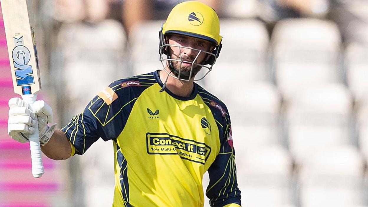 James Vince, wearing Hampshire's yellow and navy blue home shirt with yellow helmet, raises his bat on the way to a century against Essex