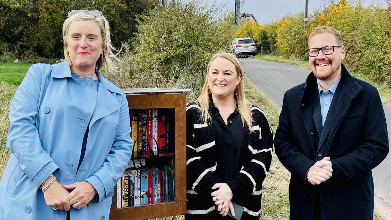 Hartlepool council leader Pamela Hargreaves, Lyndsay Hogg and MP Jonathan Brash are all standing next to a small wooden box filled with books. The box has a glass front with the Penguin Books logo on it.