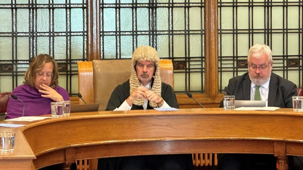 Rt Rev Tricia Hillas sitting at the horseshoe-shaped Legislative Council bench alongside the President to Tynwald Laurence Skelly and the Attorney General Walter Wannenburgh.