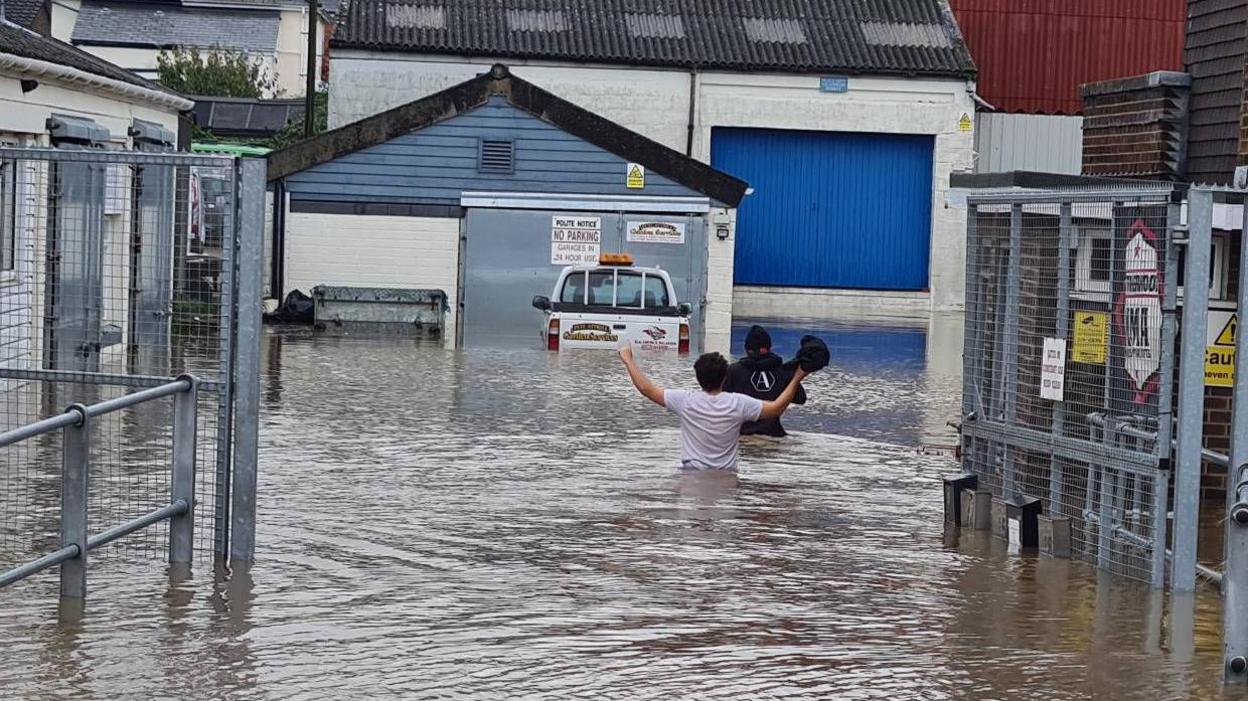 Two people wade up to their waists in flood water in a street in Ryde on 25 Oct 2023