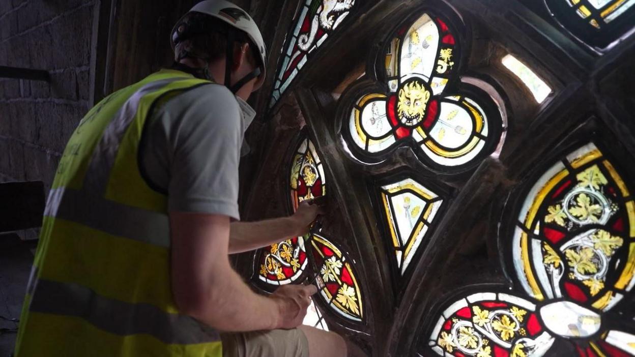 A man in hi-vis restoring the stained glass