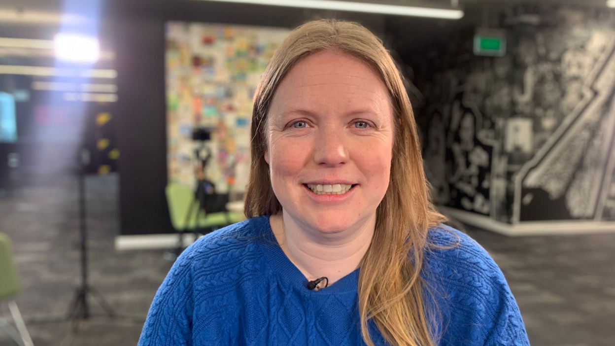 Vicky Robayna, wearing a bright blue jumper, looks straight at the camera smiling.