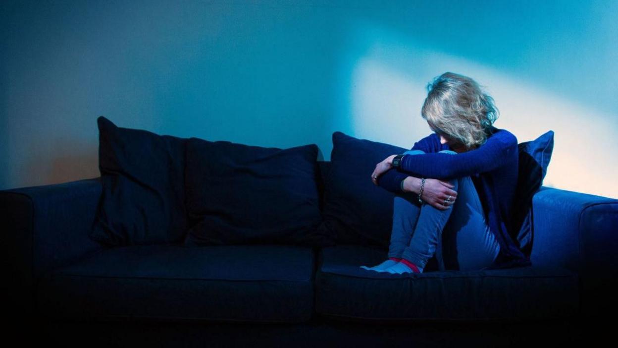 A woman with her hands around her knees on a sofa.