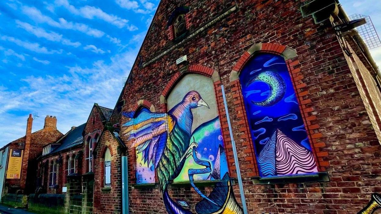 Colourful bird mural on the side of brick wall of the building on a sunny day.