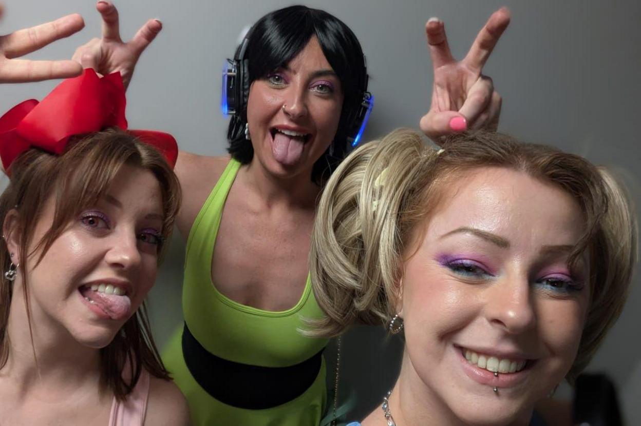 Three women stood in a row. They are all pullying silly faces and are dressed in Powerpuff girls fancy dress, while looking at the camera.