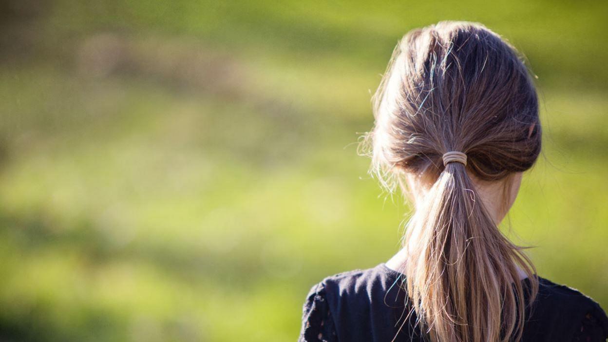 The back of a girl's head with a blonde ponytail and black top