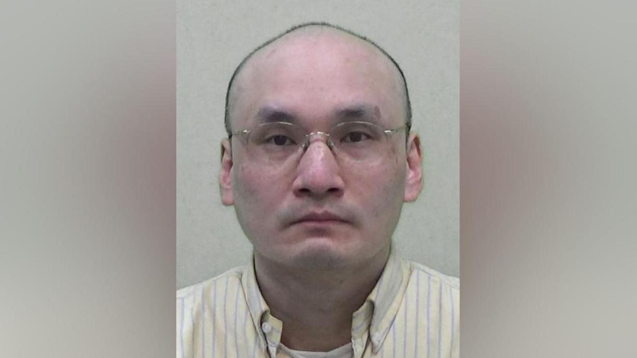 Mugshot of Kwan. he is bald and wearing glasses