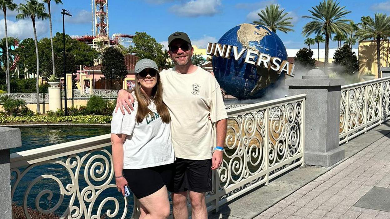 British tourists Melissa Rutter and Dan King pose for a holiday photograph in front of the famous Universal Studios globe. The couple, both wearing white t-shirts and black shorts, are smiling in the Floridian sunshine.