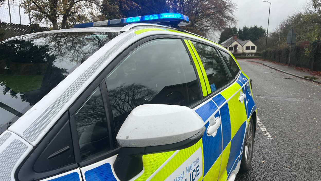 The side of a yellow, blue and white police car with its blue lights on.