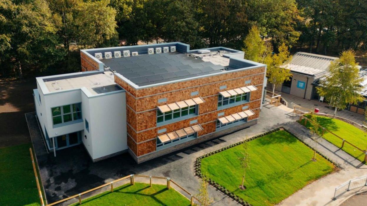 Elevated view of brick and grey render building with 9 windows and a door. There are trees and grass.