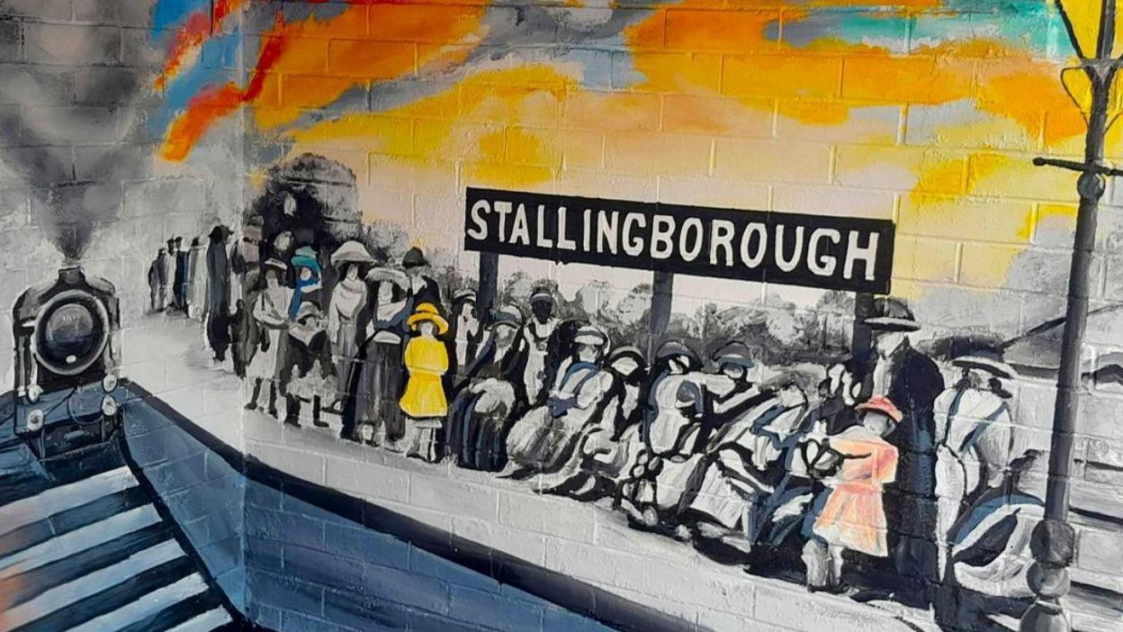 Mural of people in Victorian dress huddled together on a railway station platform. There is a locomotive in the background.