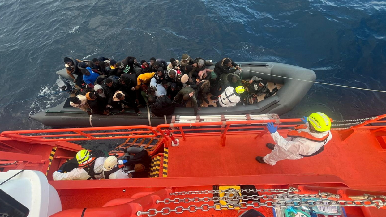 Spanish coast guards wearing white suits on a ship work on towing a rubber boat carrying migrants, including a newborn baby, off the island off the Canary Island of Lanzarote