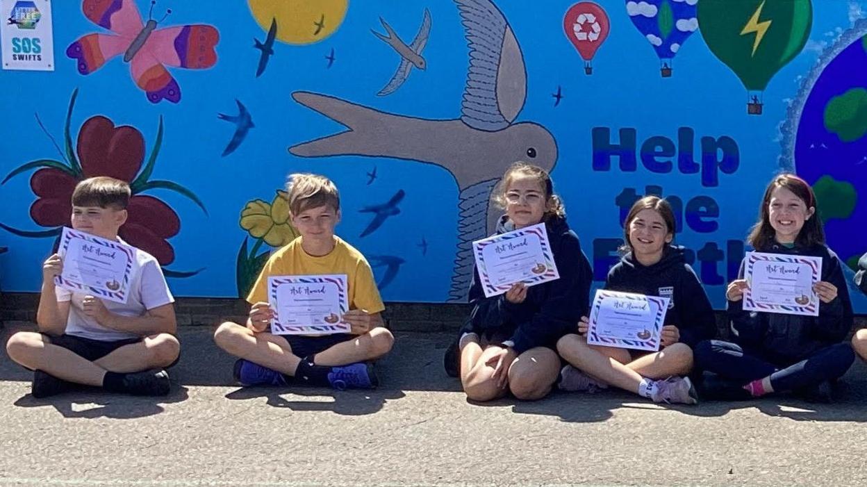 School students sitting in front of their artwork