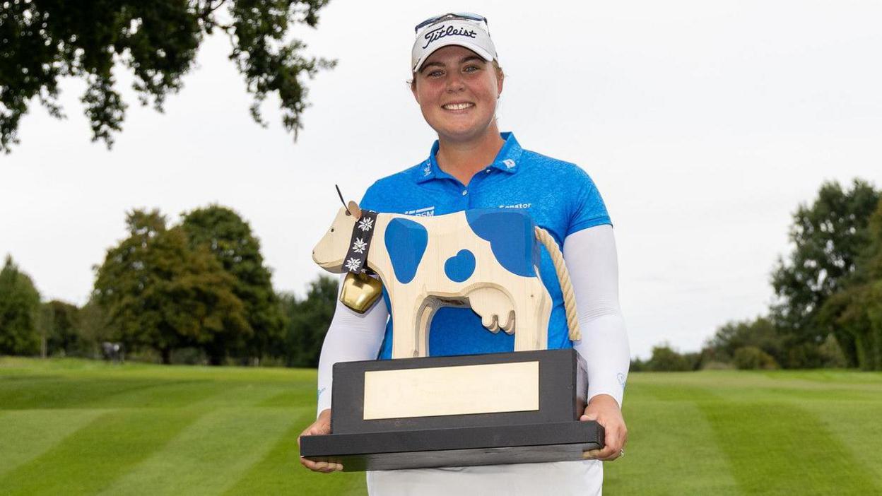 English golfer Alice Hewson smiles arsenic she holds up nan Swiss Ladies Open, which is successful nan style of a cow