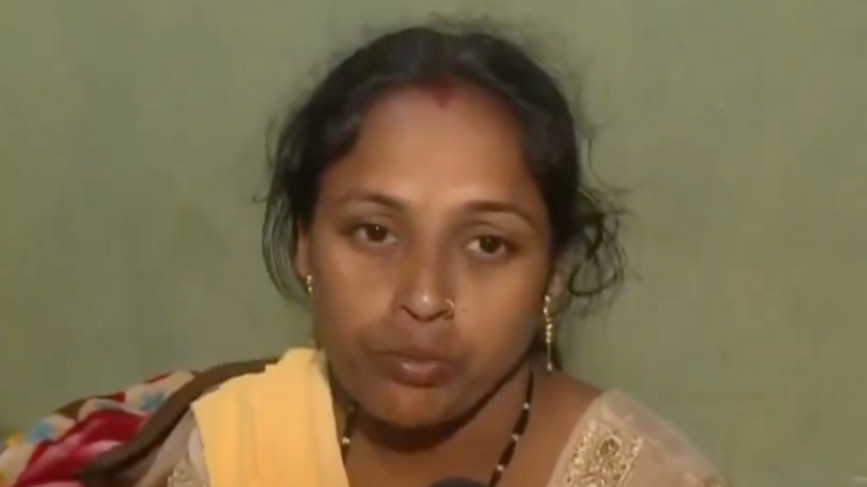 A woman wearing a yellow Indian suit looks away from the camera while speaking into a mic which has ANI written on it. 