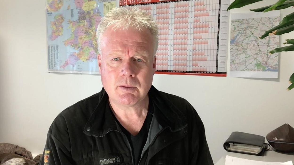 Paul Margan sitting in an office in front of a wallplanner