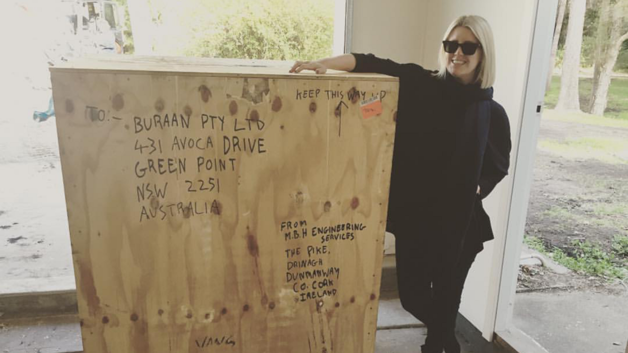 Karina Reid standing next to the crate the bell was transported in. She is leaning against the crate and smiling.