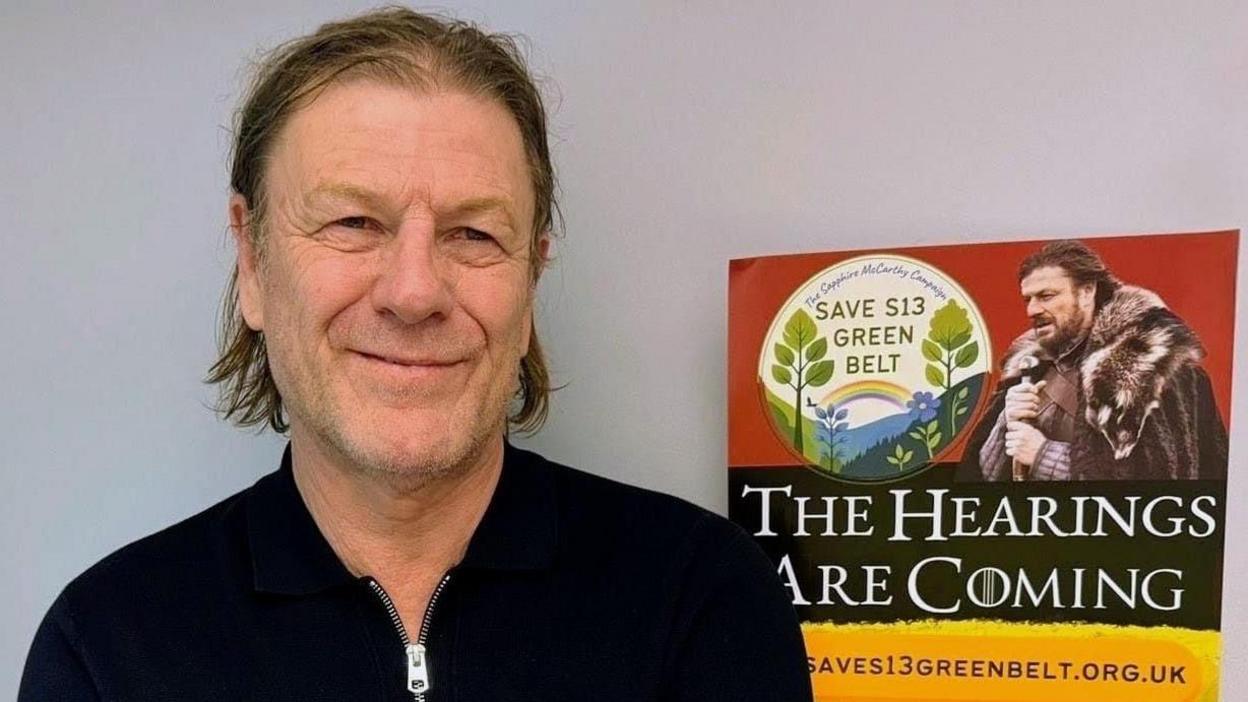 Sean Bean stood next to a poster for the "Save S13 Green Belt" campaign.