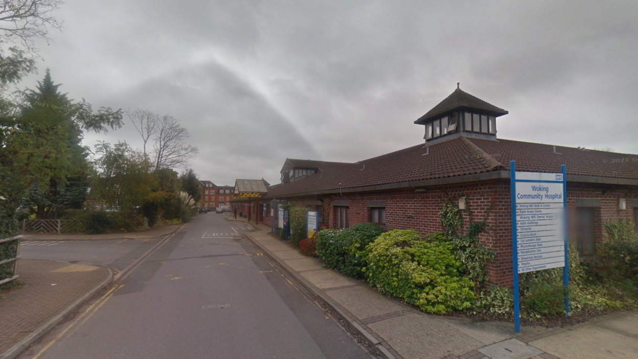 A view of the outside of Woking Community Hospital showing the main road leading to the building, along with signage.