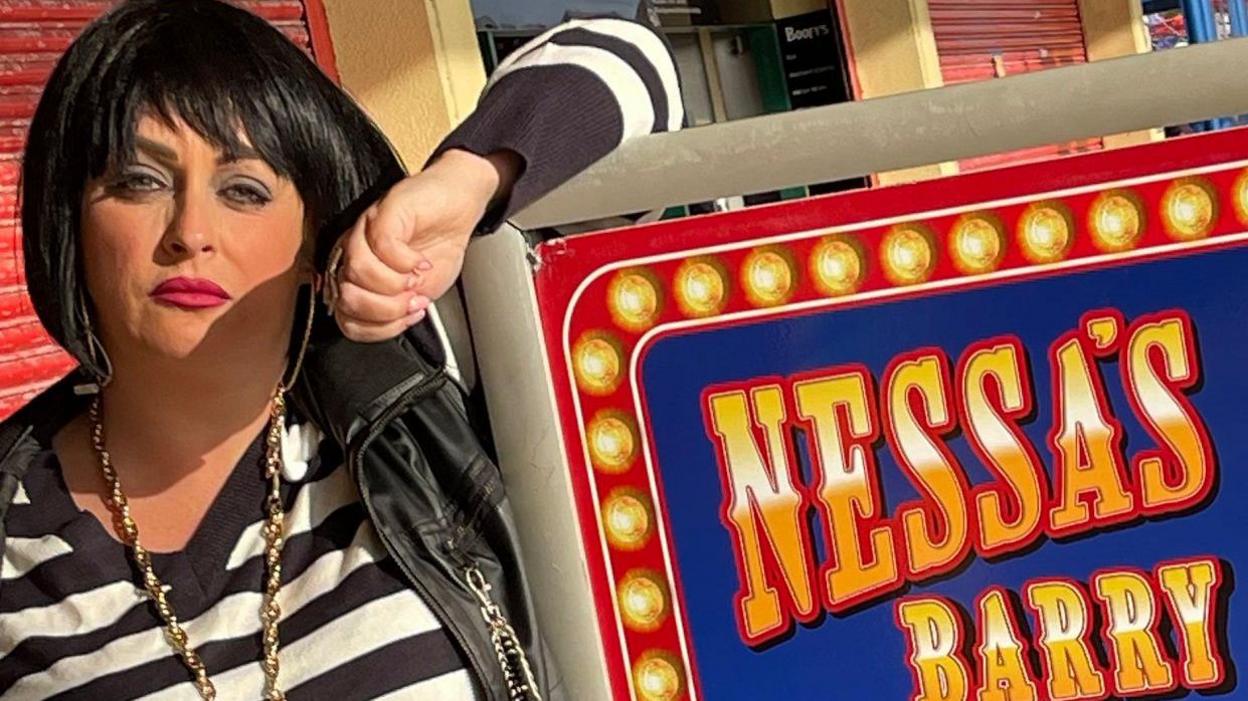 Nessa impersonator Kaz Barrett in full get up next to a sign for Nessa's Slots in Barry Island