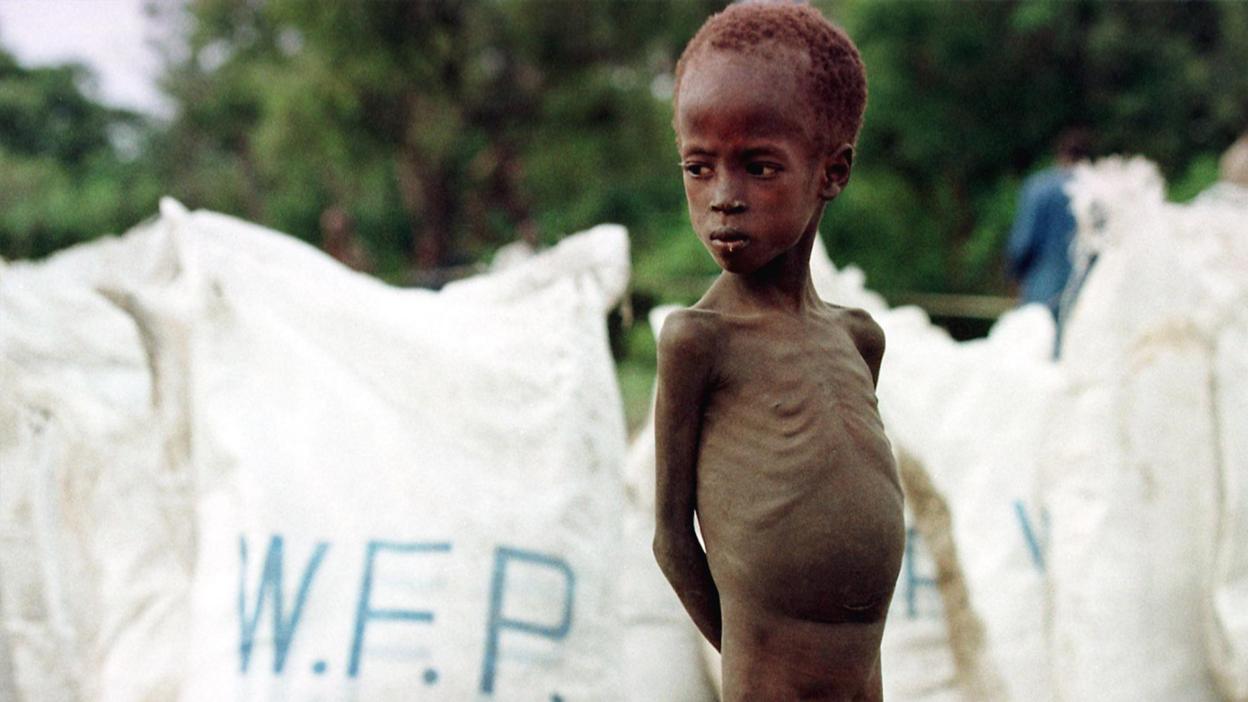 A young starving boy stands in front of relief food bags delivered by the World Food Programme on 9 August, after an airdrop by the WFP in the village of Acumcum, in the Bahr El Ghazal Province of southern Sudan