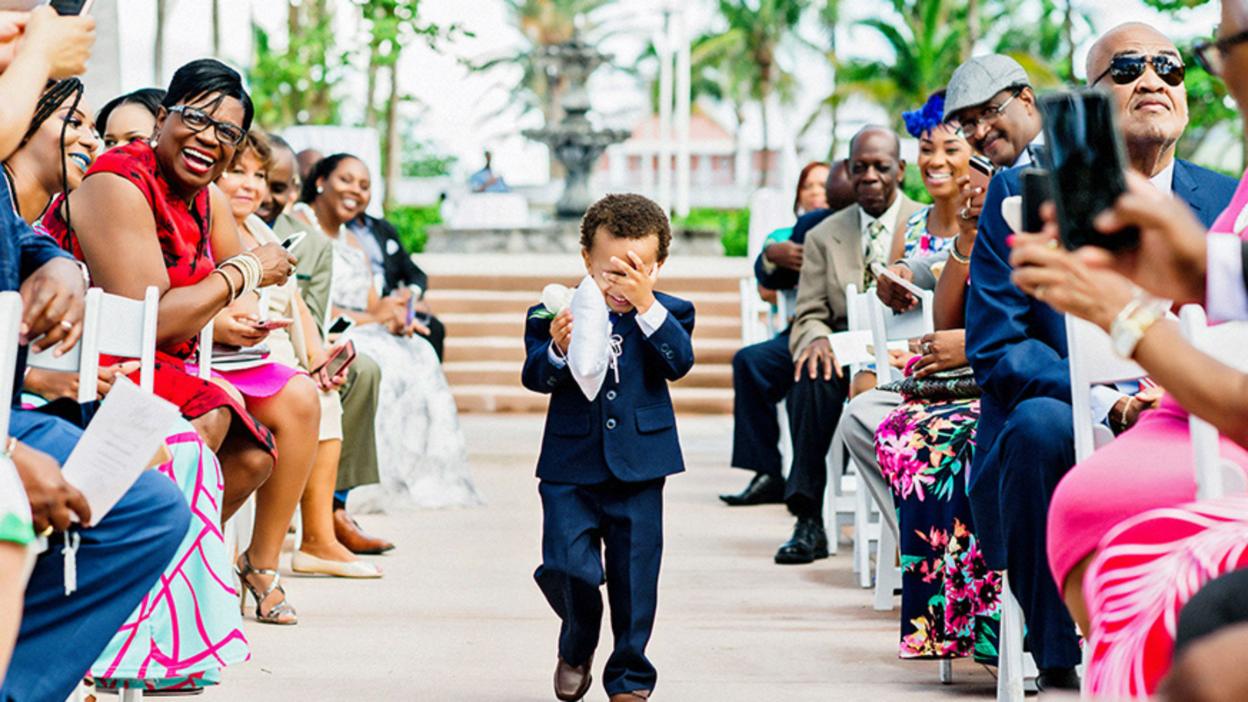 Page boy covers his face while carrying the ring cushion down the aisle at wedding