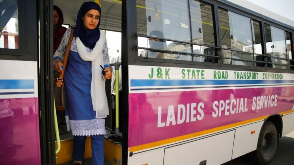 A woman in a headscarf getting off a bus marked 