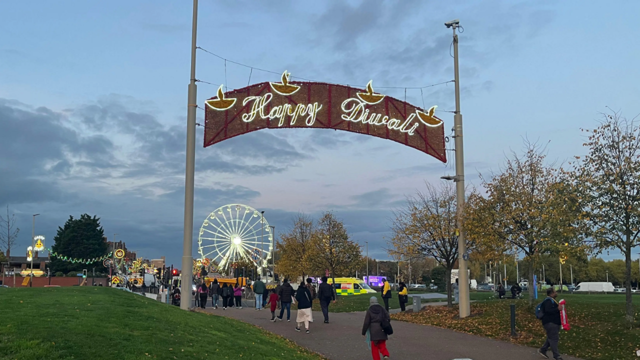 A large banner between two poles lit up saying Happy Diwali with a Ferris wheel in the back ground