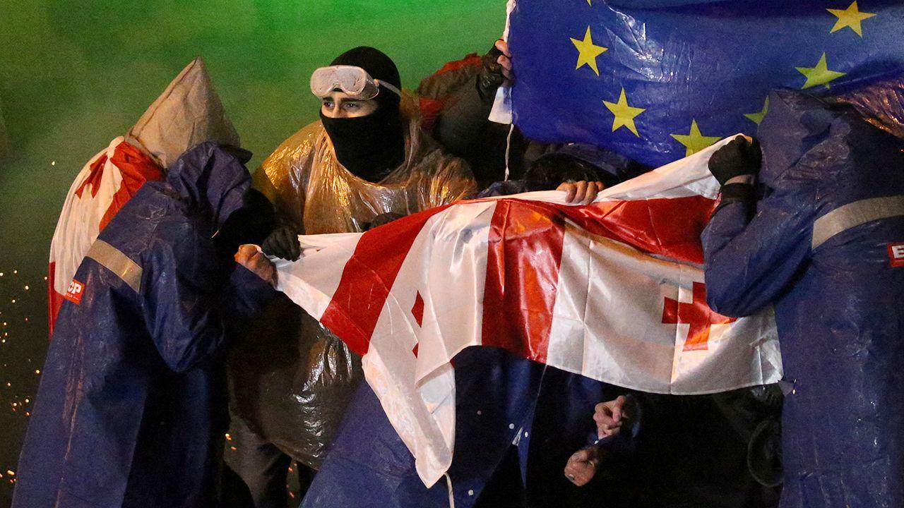 Demonstrators with Georgian and EU flags defying police water cannon in Tbilisi, 1 Dec 24