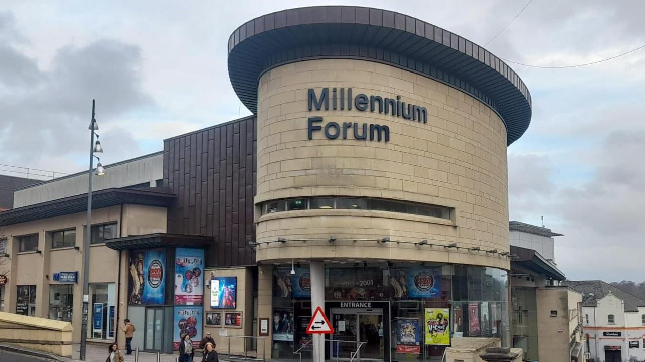 The Milenium Forum in Derry, seen from linenhall street. It has a number of promotional posters on the exterior walls. A few people walk past its front door